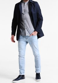 Marinblå lättviktsjacka över en mönstrad skjorta, ljusblå jeans och marinblå sneakers. Funktioner inkluderar krage, knäppt front och slim fit.