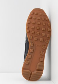 Nike-sula i brunt gummi med fyrkantiga klackar, strukturerad yta och sidologotyp; placerad mot en vit bakgrund.