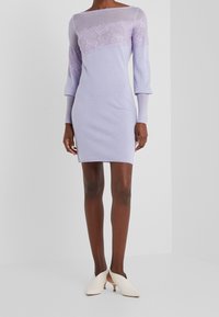 Abito lavorato a maglia lilla con maniche lunghe, caratterizzato da dettagli in pizzo intricate sul petto. Silhouette aderente, abbinato a mule color crema.