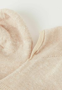 Ljust beige bomullssockor med ett texturerat stickat mönster och släta kanter, med en lätt uppvikt chiffong. Mjukt och lätt material.