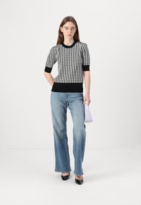 Czarny i biały sweter w wzór houndstooth z krótkim rękawem, w połączeniu z jasnoniebieskimi spodniami dzwonami i czarnymi lakierowanymi szpilkami.
