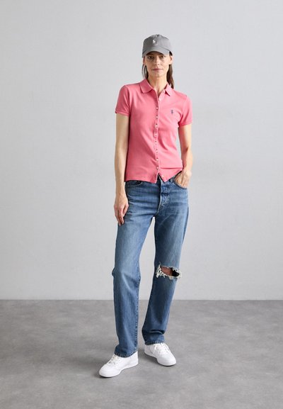 Polohemd in Hellrosa mit Knöpfen, kombiniert mit hellblauen, zerrissenen Jeans und weißen Sneakern. Eine graue Kappe rundet das Outfit ab.