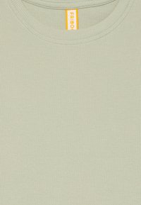 Light green ribbed fabric close-up with a round neckline and a visible yellow clothing tag inside the collar.