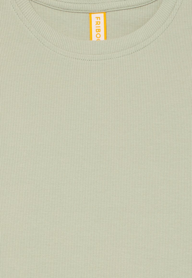 Nahtloser, hellgrüner, gerippter Stoff im Close-up mit einem runden Ausschnitt und einem sichtbaren gelben Kleidungsetikett im Kragen.