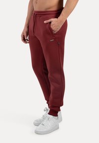 Pantalones de chándal burdeos con bolsillos laterales, cinturilla elástica y puños, combinados con zapatillas blancas. Tejido de suave mezcla de algodón.