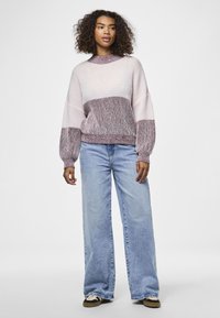 Maglione lavorato a maglia con blocchi di colore orizzontali in rosa chiaro e bordeaux, con maniche larghe e una texture a coste. Abbinato a jeans blu larghi.