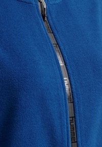 Blå fleecetröja med dragkedja, med grå dragkedjesnor med "hummel"-logotyp, slät textur och design med ståkrage.