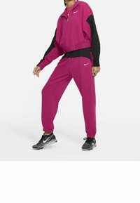 Rosa och svart träningsdräkt med en zip-up jacka och elastiska ärmslut, tillsammans med svarta och silverfärgade sneakers, med Nike-logotyp.