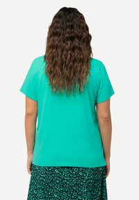 Camiseta de manga corta color turquesa con un ajuste relajado, combinada con una falda verde con estampado de leopardo. Tejido de algodón suave; la vista trasera muestra cabello con textura de olas.