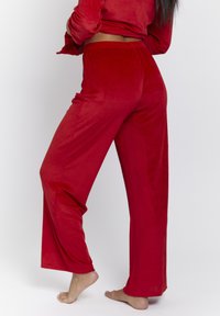 Red ribbed loungewear set features a long-sleeve top and wide-leg pants. The fabric is soft with a subtle texture and comfortable fit.