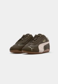 Par de zapatillas Puma marrones con acentos laterales rosa claro, cordones y suelas de goma, presentadas sobre un fondo blanco.
