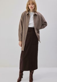 Pikk pruun seelik, millele on sobitatud beežist villast nööpidega särk ja valge topp. Komplektis on struktuurne siluett ja kaks eesmist taskut.