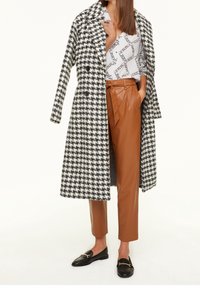 Sort og hvid houndstooth frakke, en-knaps, kombineret med højtsiddende brune læderbukser og sorte loafers.