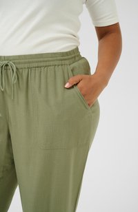 Green, lightweight, woven pants with an elastic waistband and drawstring. Side pockets and a relaxed fit. Textured fabric visible.