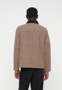 Barna kockás zakó kontrasztos sötét gallérral, dobozos szabással, hosszú ujjakkal és egyenes szegéllyel, hátulnézetből bemutatva.