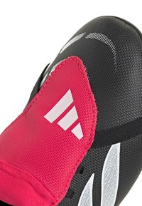 Κοντινό πλάνο ενός μαύρου και ροζ αθλητικού παπουτσιού με λευκό λογότυπο Adidas και λεπτομερή υλικά με υφή.