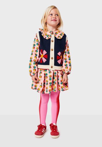 Conjunto multicolorido que presenta un chaleco azul marino con un diseño floral, un vestido rosa con estampado y mallas rosas. Zapatillas rojas completan el look.