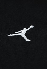 Tecido preto com o logótipo Jumpman bordado em branco, representando um atleta no ar, estendendo os braços e as pernas numa pose dinâmica.