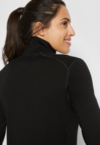 Czarny sweter z wysokim kołnierzem, wykonany z gładkiego materiału. Ma dopasowany krój z subtelnymi przeszyciami wzdłuż ramion.