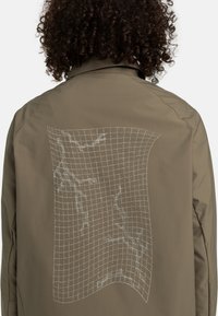 Olive green jacket featuring a grid-patterned graphic in white on the back. The fabric has a smooth, matte texture and a modern design.