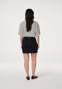 Gestreepte top met korte mouwen in crème en marineblauw, gecombineerd met een zwarte rok met een ritssluiting aan de achterkant. Model draagt donkere, versierde loafers.