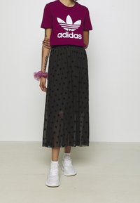 Magenta bomulls t-shirt med vitt Adidas-logga, ihop med en svart maxikjol i tyll med stjärnmönster och vita sportskor.