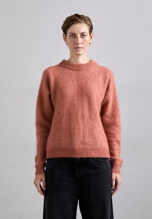 Overstor størrelse, rundhalset genser i myk, teksturert korallull. Har ribbestrikkede mansjetter og kant, kombinert med mørke, vide jeans.