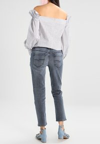 Blusa de rayas con hombros descubiertos y mangas abullonadas, combinada con jeans de un azul claro y zapatos de tacón azul con acentos florales.