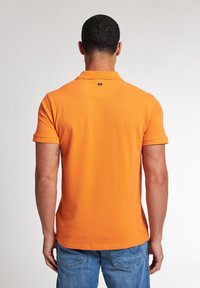 Oranžová polokošile s jemnou texturou, krátkými rukávy a klasickým límcem. Na zadní straně u výstřihu se nachází štítek značky.