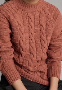 Różowy sweter z dzianiny, z splotem warkoczowym, okrągłym dekoltem oraz ściągaczami na rękawach i u dołu, wykonany z teksturowanej, ciepłej tkaniny.