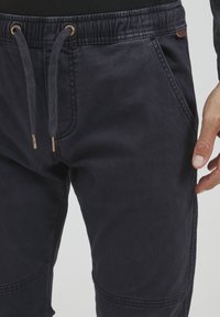 Marineblå joggingbukser lavet af bomuldsblanding, med elastisk talje, snørebånd, sidelommer og dekorative sømme langs sømmene.