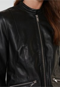 Zwarte leren motorjack met een staande kraag, zilveren ritsen en zijzakken. Heeft een gladde textuur en een getailleerde pasvorm.