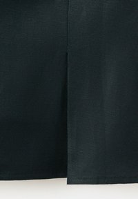 Lähikuva tummasta kankaasta, jossa on keskellä pystysuora sauma ja näkyvä tekstuuri, esittäen vaatteen alahelmaa.