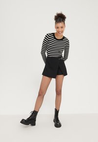Haut à rayures noir et blanc à manches longues, jupe portefeuille noire avec bouton, collants en résille, et bottes de combat noires à lacets.