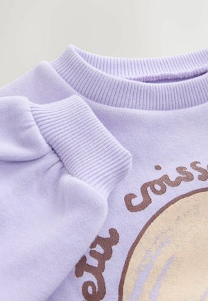 Fliederfarbenes Sweatshirt mit geripptem Rundhalsausschnitt und Bündchen, versehen mit einem runden Aufdruck mit dem Schriftzug "Croissant" sowie strukturierten Details in Braun und Gold.