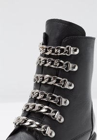 Czarne botki za kostkę z metalicznymi detalami wzdłuż sznurowadeł, wykonane z gładkiej skóry o matowym wykończeniu i solidnej podeszwie.