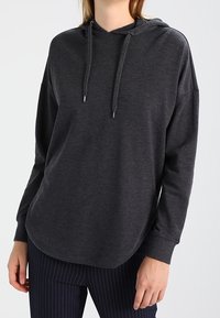 Felpa grigia scura realizzata in tessuto morbido, dotata di cappuccio con lacci, spalle scese e orlo arrotondato. Abbinata a pantaloni a righe.