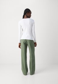 White long-sleeve top with a fitted design, paired with high-waisted, wide-leg green trousers, showcasing a smooth texture and minimal detailing.