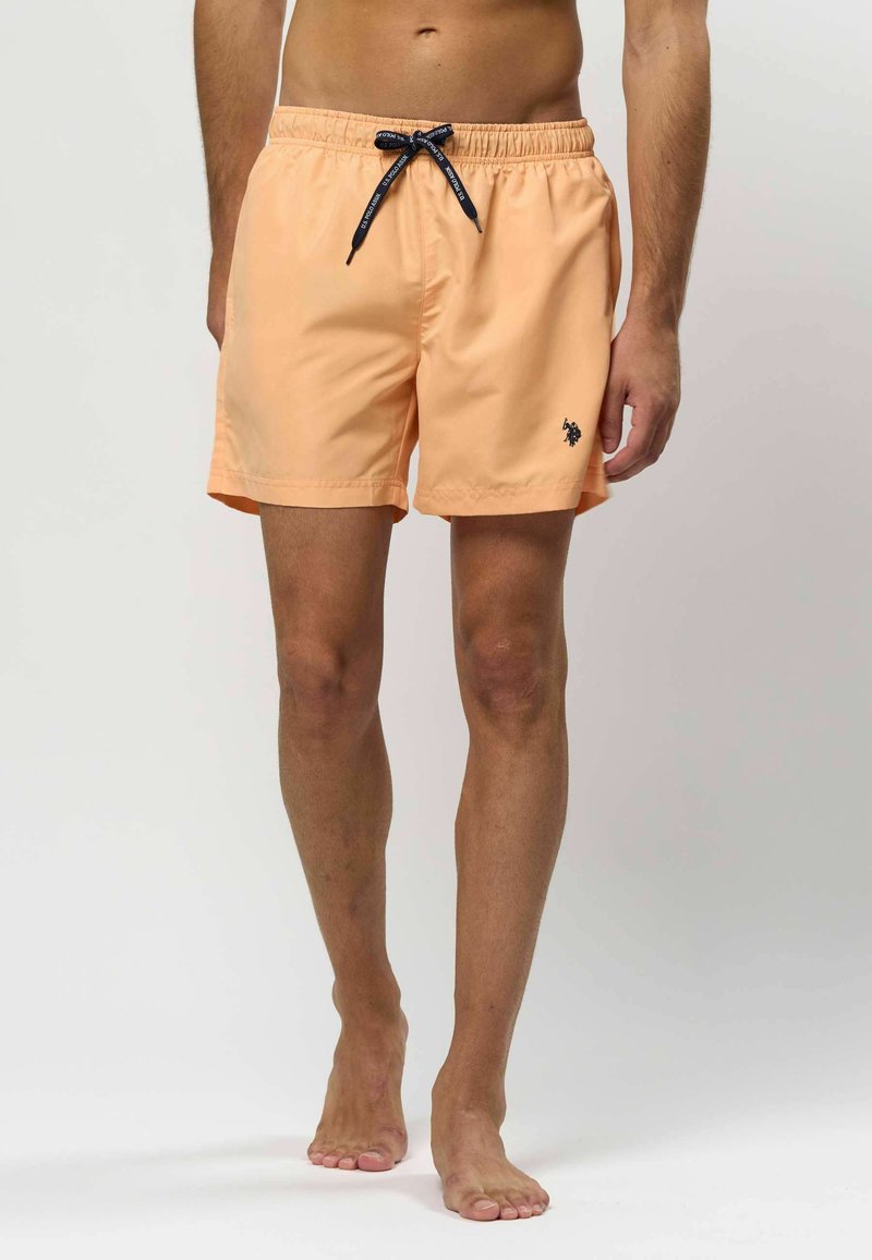 Perzik zwemshorts met een elastische tailleband, zwarte trekkoord en kleine logo-accent. Glad materiaal, knielange snit, lichtgewicht ontwerp.