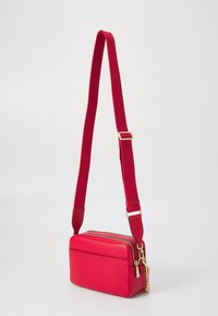 Borsa a tracolla rossa con finitura texturizzata, due scomparti con zip, un accento in catena dorata rimovibile e una tracolla regolabile in tessuto.