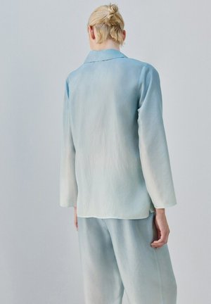 Person with blonde hair in a loose bun wearing a light blue ombre long-sleeve top and matching pants, facing away against a plain gray background.