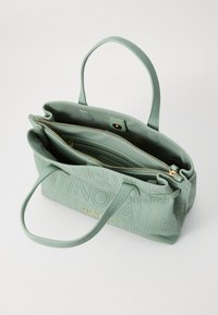 Šviesiai žalia pirkinių krepšys, pagamintas iš tekstūruoto audinio, su iškiliais rašmenimis, auksinėmis detalėmis ir dviem vidiniais skyriumi, užsegamais užtrauktukais.