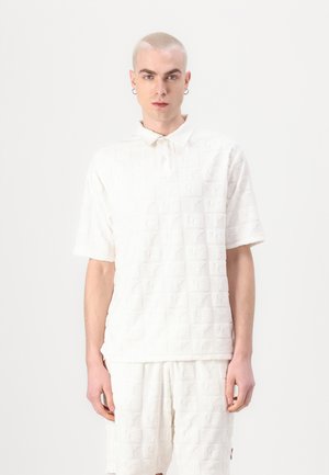 White short-sleeve polo made of textured fabric featuring repeated logo patterns, with a buttoned collar and relaxed fit.