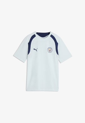 Φανέλα ποδοσφαίρου της Manchester City σε ανοιχτό μπλε χρώμα με σκουρόχρωμες μπλε περιοχές στους ώμους, λογότυπο Puma στη δεξιά πλευρά του στήθους και έμβλημα του συλλόγου στην αριστερή πλευρά του στήθους.