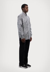 Long-sleeve button-up shirt in gray with a textured snake print. Paired with black jeans and black sneakers featuring white accents.