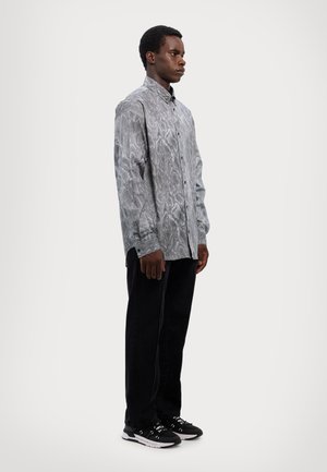 Chemise à manches longues avec boutons en gris, ornée d'un motif de serpent texturé. Associée à un jean noir et des baskets noires avec des accents blancs.