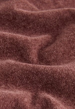 Pehmeä, tekstuurinen, mauve-väriinen kangas, jossa on hienovarainen kiilto, ja joka esittää helliä aaltoja ja taitoksia. Materiaali vaikuttaa lämpimältä ja mukavalta.