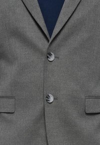 Grauer Blazer aus einem glatten Stoff, mit zwei vorderen Knöpfen und zwei Taschen sowie einem Revers mit Notchdesign. Darunter befindet sich ein navyblaues Hemd.