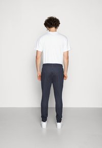 White t-shirt and navy pinstripe pants with elastic cuffs and white sneakers. The fabric appears smooth, with a contrasting pattern.