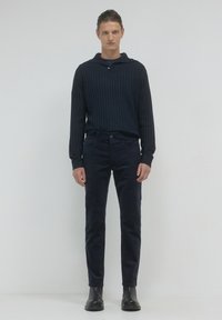 Haut à manches longues côtelé bleu marine avec patte de boutonnage, associé à un pantalon slim bleu marine et des bottines noires, sur fond neutre.